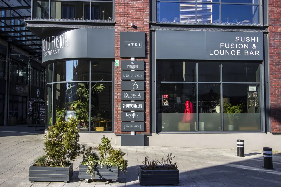 Exterior: facade of the Jatki building corner with Sushi Fusion and Lounge Bar signage, red brick, directory board, and planters