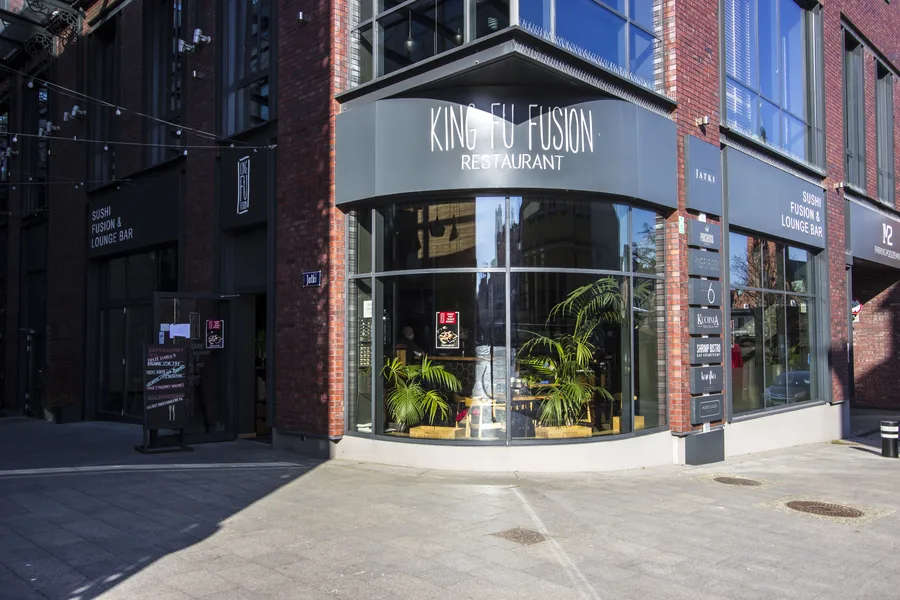 Exterior: corner facade with King Fu Fusion Restaurant signage, curved glass corner, red brick Jatki building, and palm plants visible inside