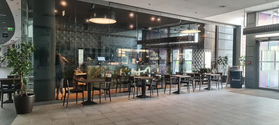 Detail: through-glass exterior photograph from unique right-side angle showing the reversed perspective of the built 72 square metre sushi restaurant with entrance, 3D Decus Bent sculptural wall, and disc pendant