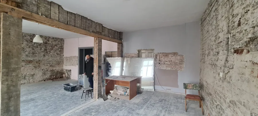 Interior: site survey showing stripped interior with exposed brick wall, timber beam structure, and raw concrete floor before apartment fit-out