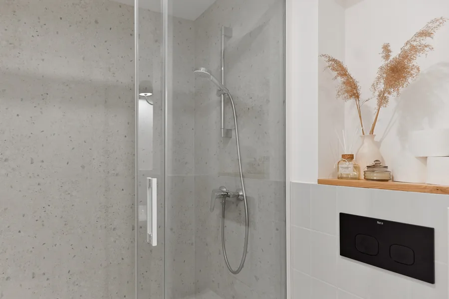 Detail: terrazzo shower wall and floor with honed aggregate finish, recessed shower niche, and matte black rain shower head in Apartment A bathroom