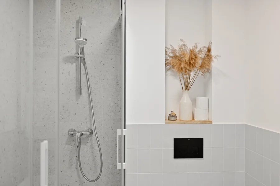 Detail: shower niche with terrazzo tile surround, matte black fixtures, and textured stone-effect wall tiles in Apartment B bathroom