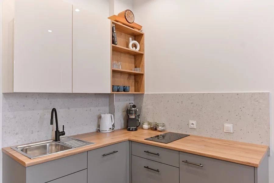 Detail: kitchen materials close-up showing timber countertop edge, ceramic backsplash tiles, and matte black cabinet hardware against exposed brick