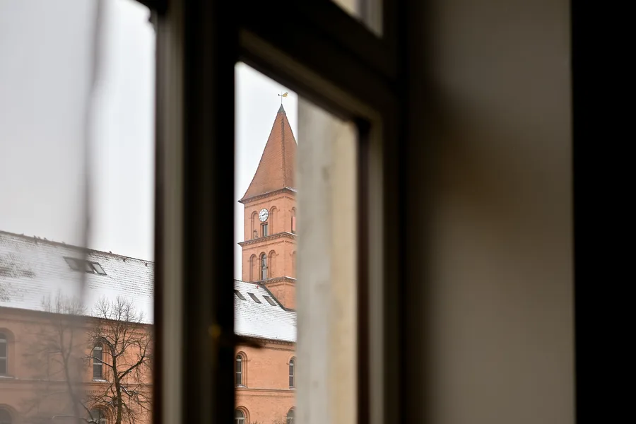 Detail: window view of medieval Torun church tower through apartment window with brick mullion visible, connecting interior design to historic context