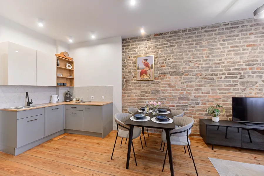 Interior: Apartment A kitchen-dining area with oak table, pendant lighting, exposed brick accent wall, and open-plan connection to living zone