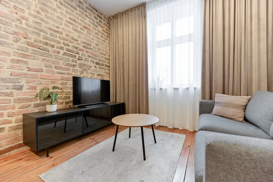 Interior: Apartment A bedroom with oak headboard wall, white bedding, pendant lights, and exposed brick column creating intimate sleeping alcove