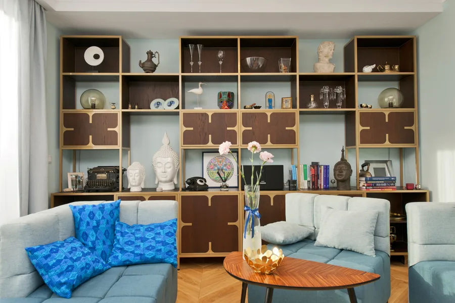 Living room frontal view with custom dark wood bookshelving wall with brass detail panels, teal modular sofa, mid-century oval coffee table, and herringbone parquet