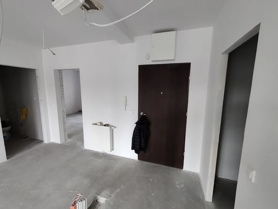 Before: shell apartment interior with large windows, concrete floor, radiator visible, and river promenade view through balcony door at Jagiellonska 36B