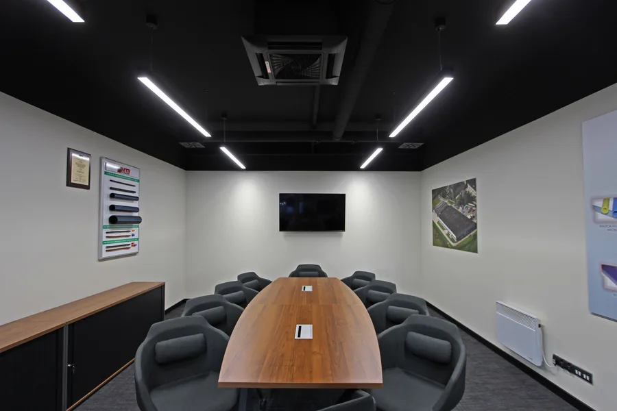 Interior: conference room frontal view down walnut boardroom table with 12 grey chairs, linear LED ceiling, exposed HVAC, and MTB product sample board