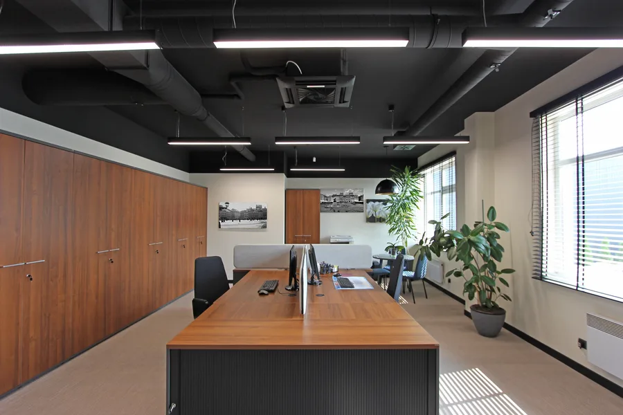 Interior: private office reverse angle showing walnut wardrobes prominent, black-and-white city photography on wall, round meeting table, and rubber tree plant