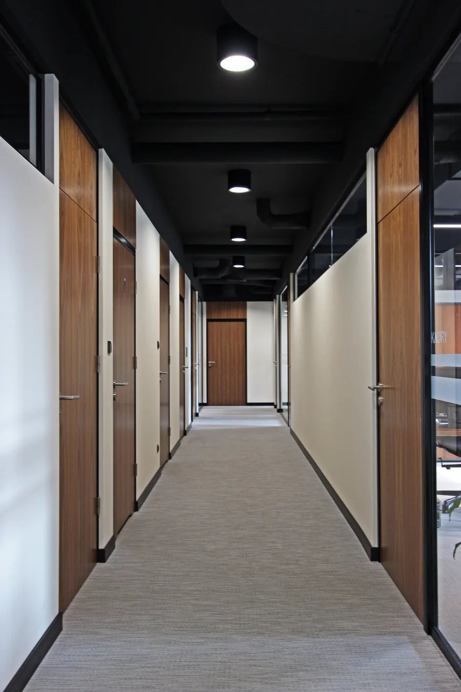 Interior: corridor with glass partition showing meeting nook with blue chairs and gold pendant, and lounge with Grace furniture and botanical prints beyond