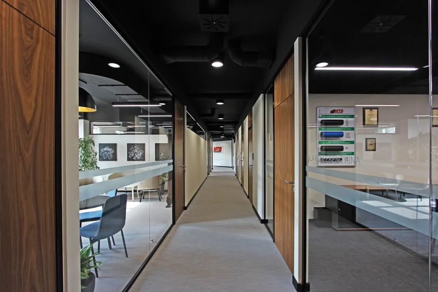 Interior: corridor looking into executive office through glass showing antique carved coat rack, vintage chairs, deer antler artwork, and heritage furnishings