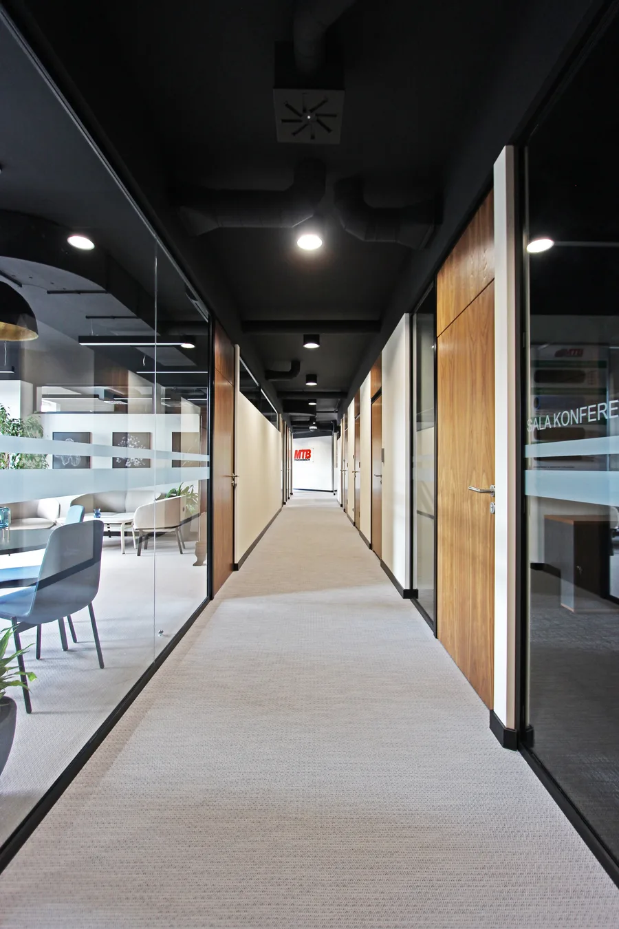 Interior: open-plan workspace wide shot from meeting nook with gold dome pendant foreground, glass partitions, workstation islands, walnut desks, and plants