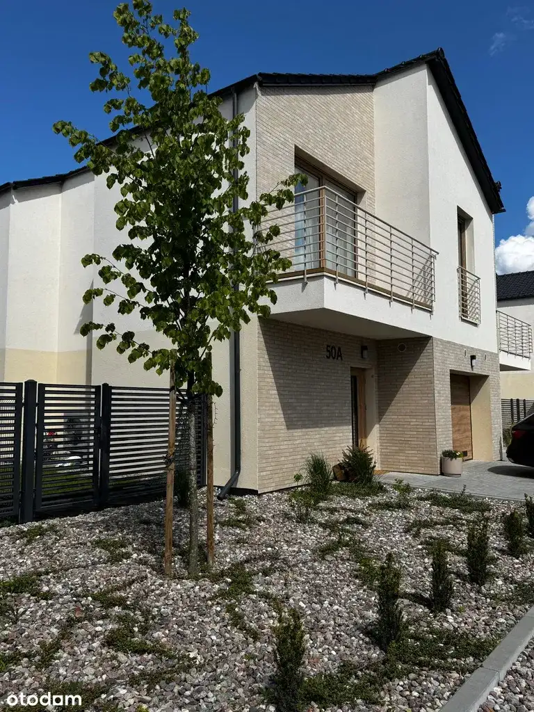Close-up realization photo of unit 50A front facade showing clinker brick to white render material transition, metal railings, and gravel garden landscaping