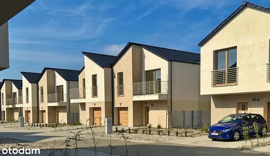 Ground level street perspective photo showing rhythmic row of houses with blue Hyundai bearing Urban Space developer branding parked on internal road