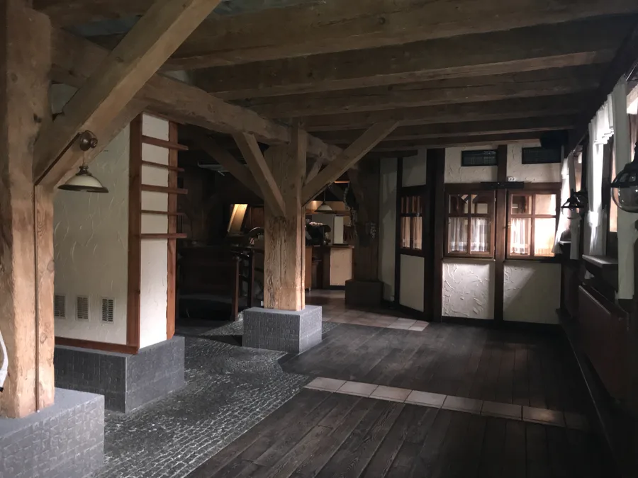 Documentary: before-renovation interior photograph showing the existing dark-stained half-timber szachulcowa structure, heavy wooden furniture, and old indoor water channel with bridge railings in Port 13 restaurant