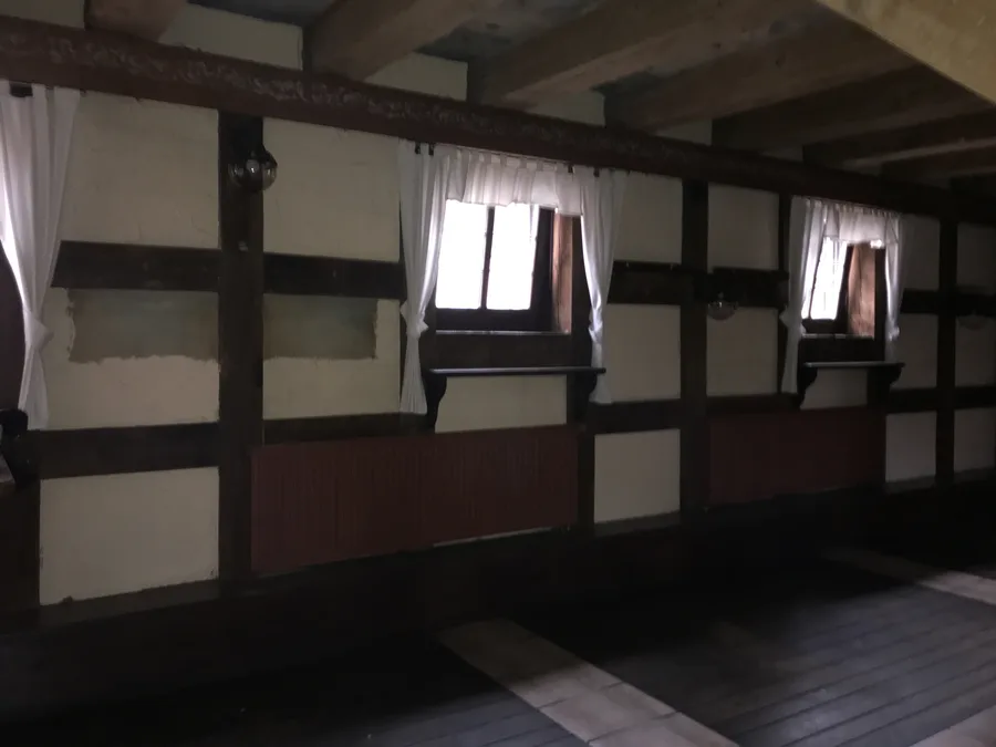 Documentary: before-renovation photograph showing the original szachulcowa timber-frame wall with white plastered infill panels and curtained windows in the dark heavy interior of the old Port 13