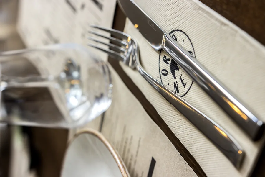 Branded cloth napkin with embroidered Orso Nero circular emblem folded with polished cutlery on oak table surface