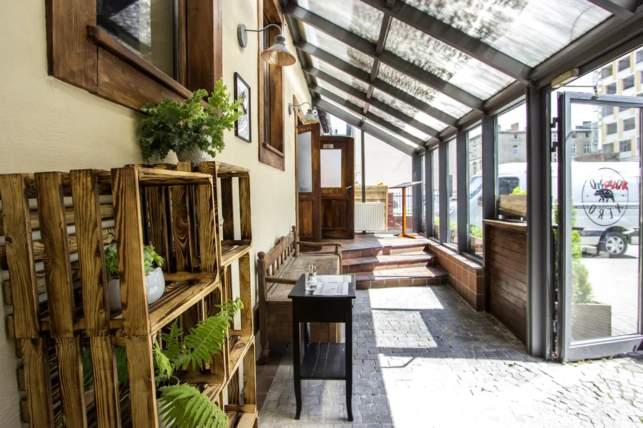 Covered vestibule with cobblestone floor, antique wooden bench, glass roof overhead, and terracotta threshold marking the transition from street to restaurant