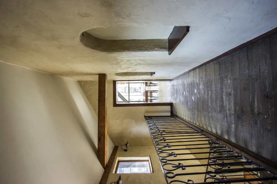 First floor stairwell arrival showing the transition from microcement landing to reclaimed timber floor with rattan pendants ahead