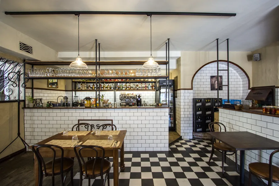 Ground floor evening atmosphere with warm pendant lighting over the bar counter, bottle display glowing, and timber ceiling above