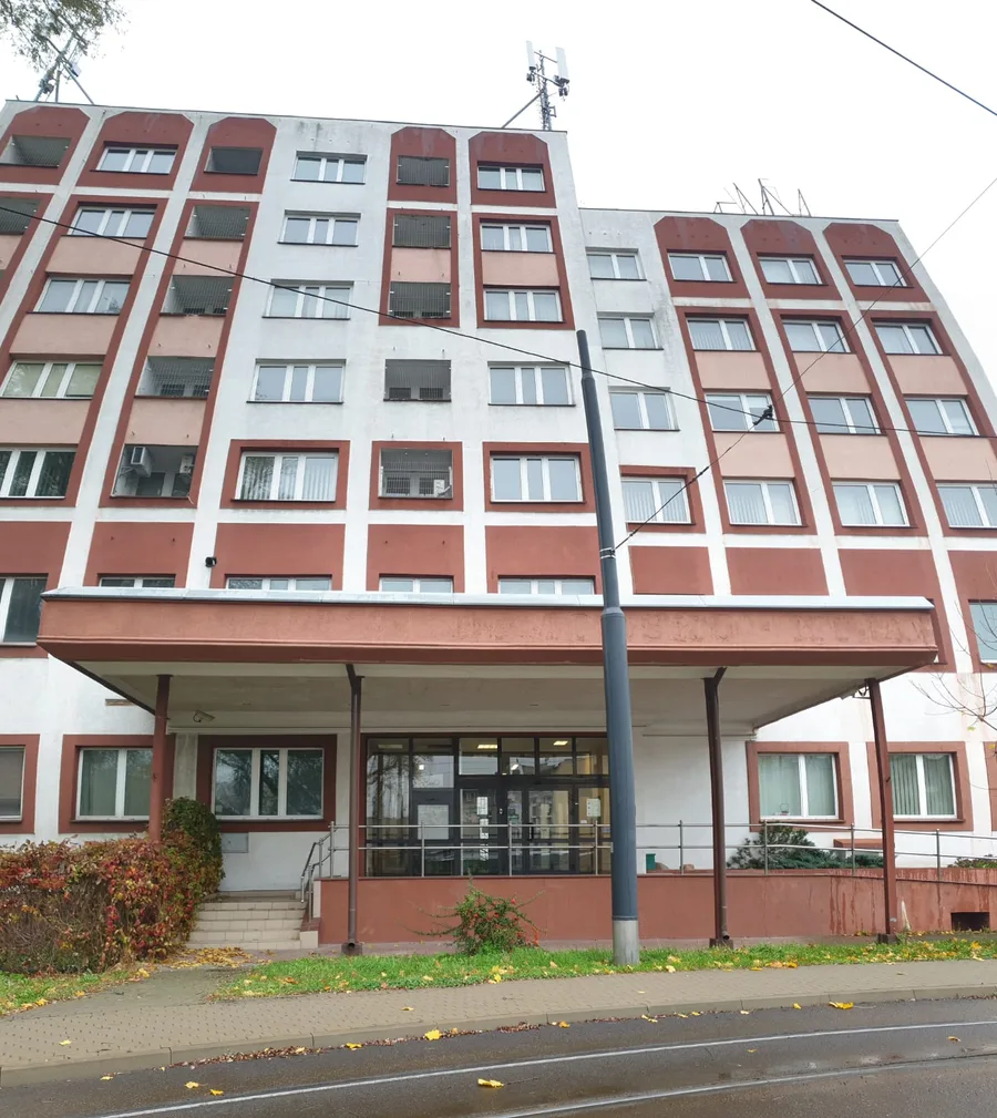 Documentary: head-on facade photograph of the existing 1975 Soviet-era workers hotel showing all seven floors with the original red and white facade, entrance canopy, and rooftop antenna before conversion
