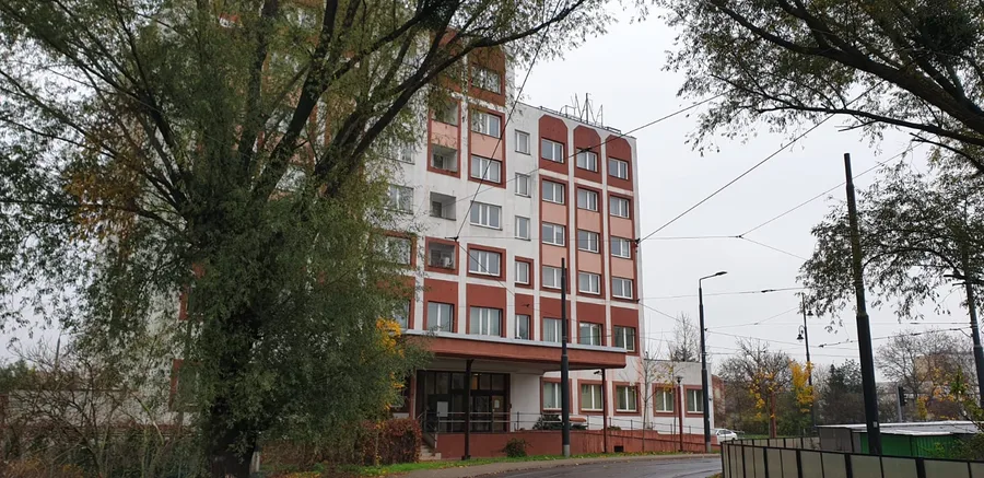 Documentary: full building street photograph with tram tracks showing the red and white Soviet-era facade of the former hotel robotniczy before its conversion to student dormitory housing