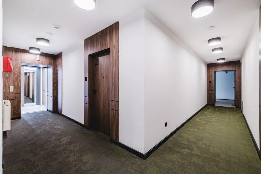 Hotel corridor with green patterned carpet, walnut apartment doors