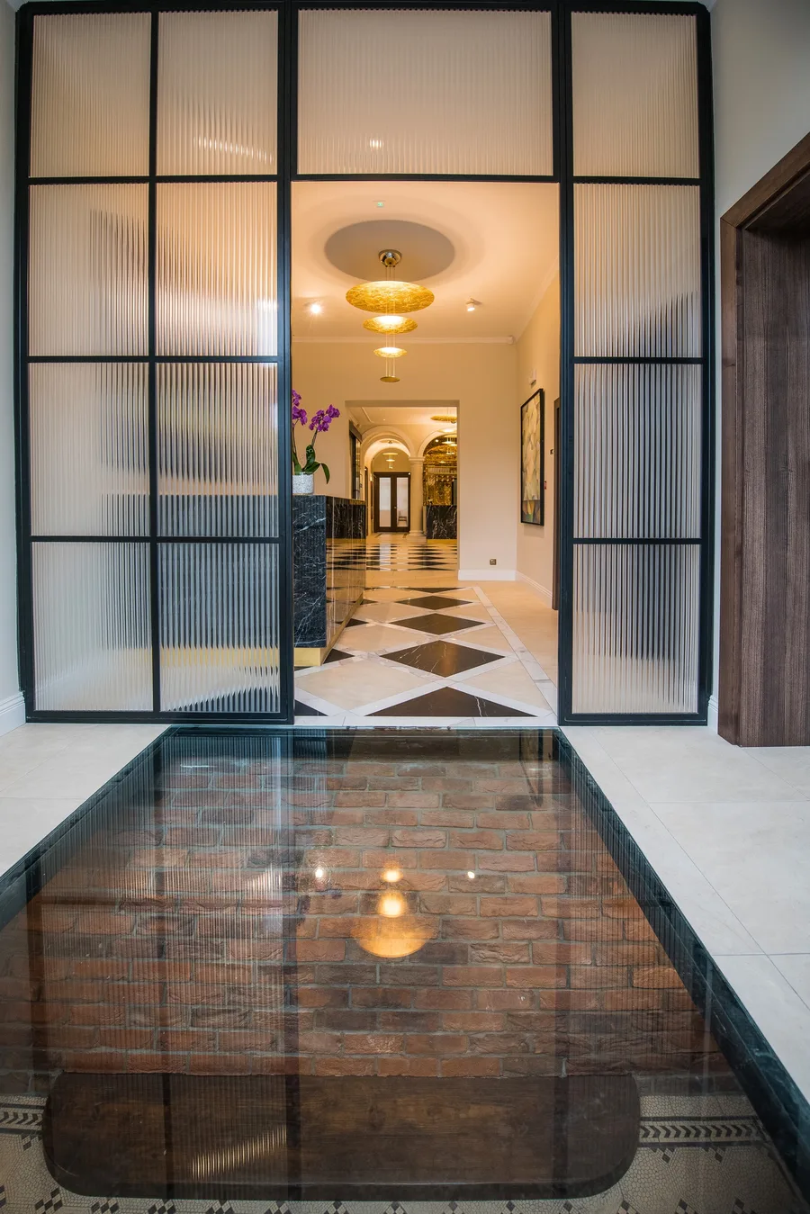 Glass floor revealing original brick foundation below through black steel-frame doorway — unique architectural feature