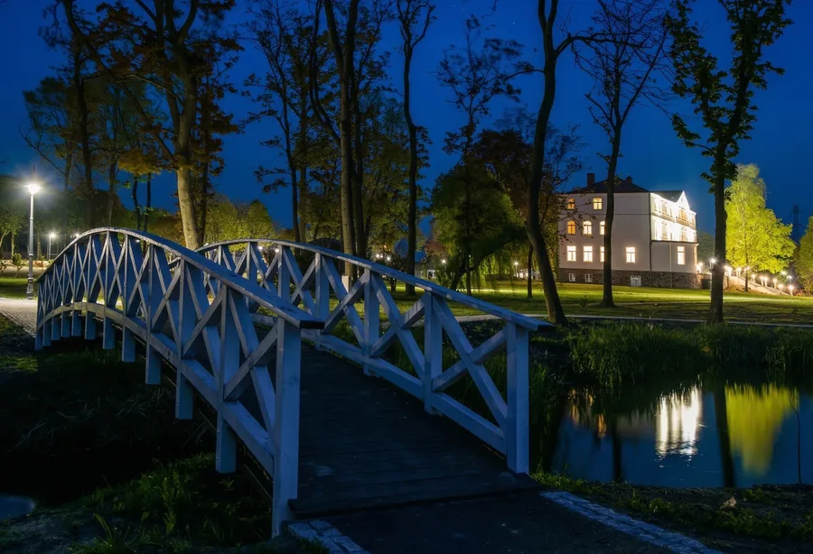 Night view of white wooden bridge with palace illuminated in background and pond reflection