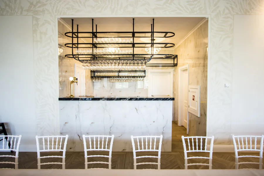 Orangerie marble bar with glass rack overhead, chiavari chairs, and botanical wallpaper
