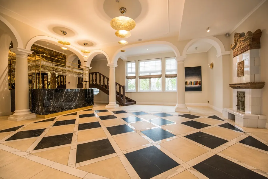 Grand lobby with marble reception desk, black-and-white diamond checkered floor, gold pendant chandeliers, and ornamental staircase in the restored 1906 palace