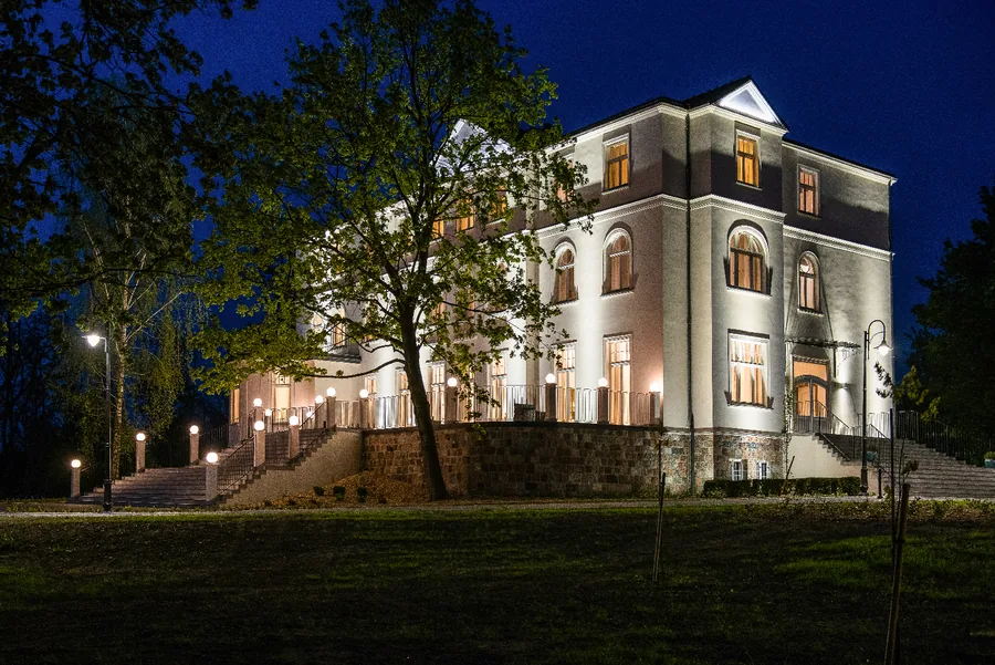 Palace illuminated at night from park side with warm ground-floor glow through windows