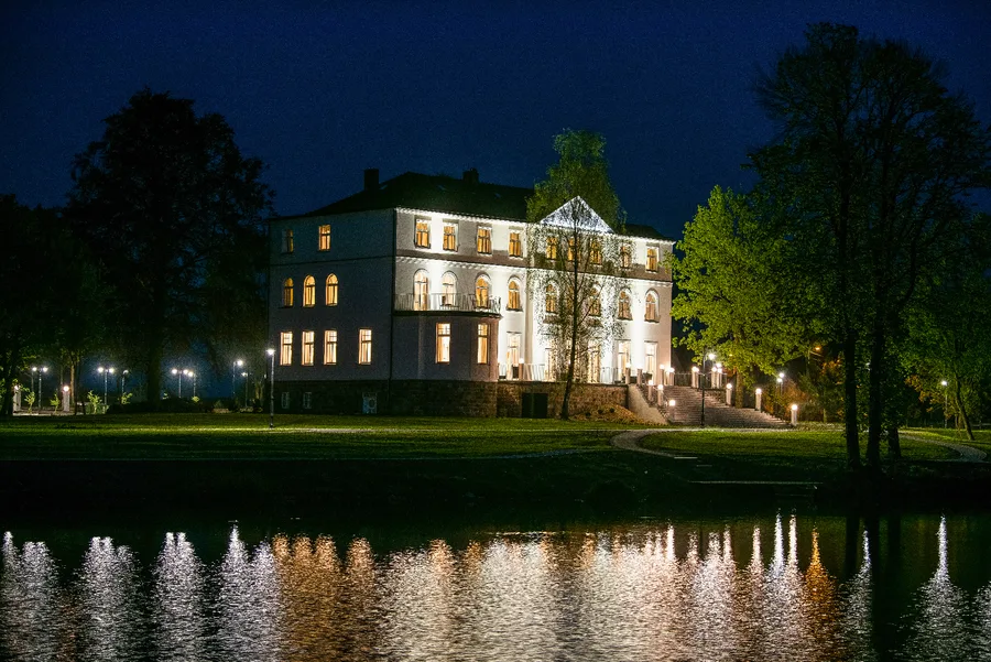 Palace reflected in lake at night with illuminated windows creating mirror image across still water