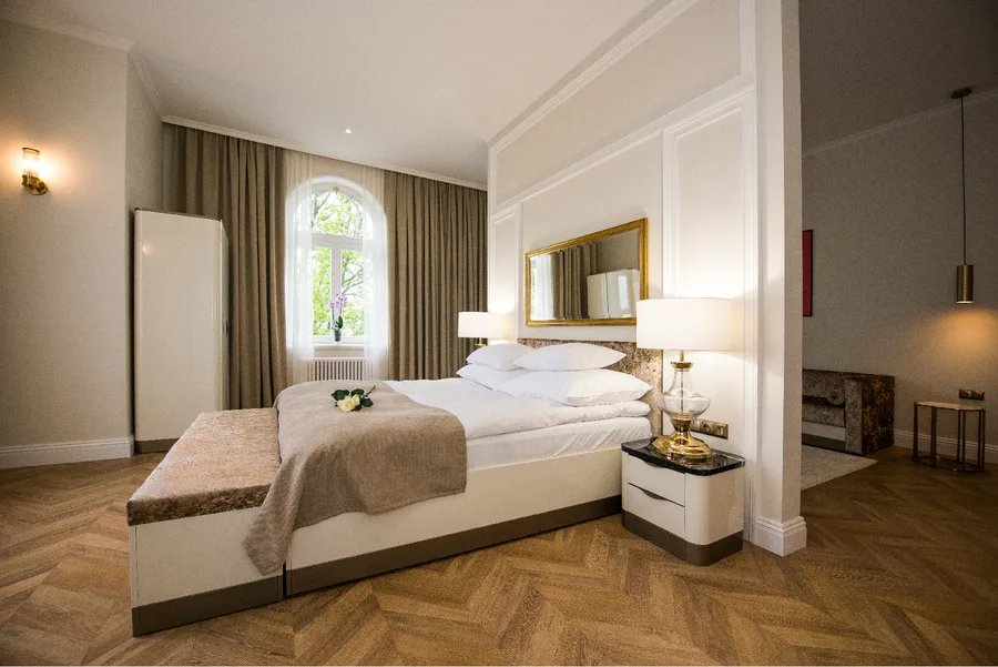 Hotel suite bedroom with white bed, gold-framed mirror, and heritage proportions