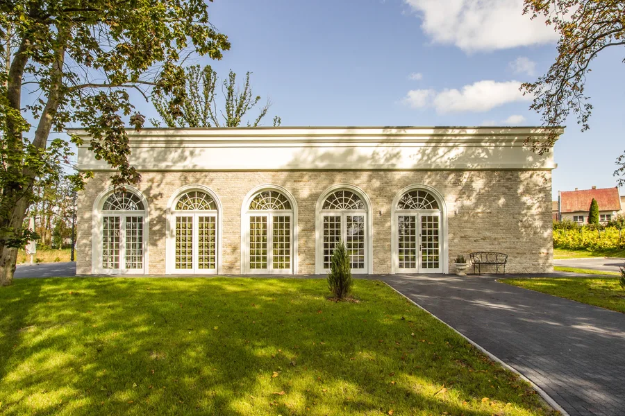 Orangerie ballroom exterior from park with stone facade, arched windows, and garden path