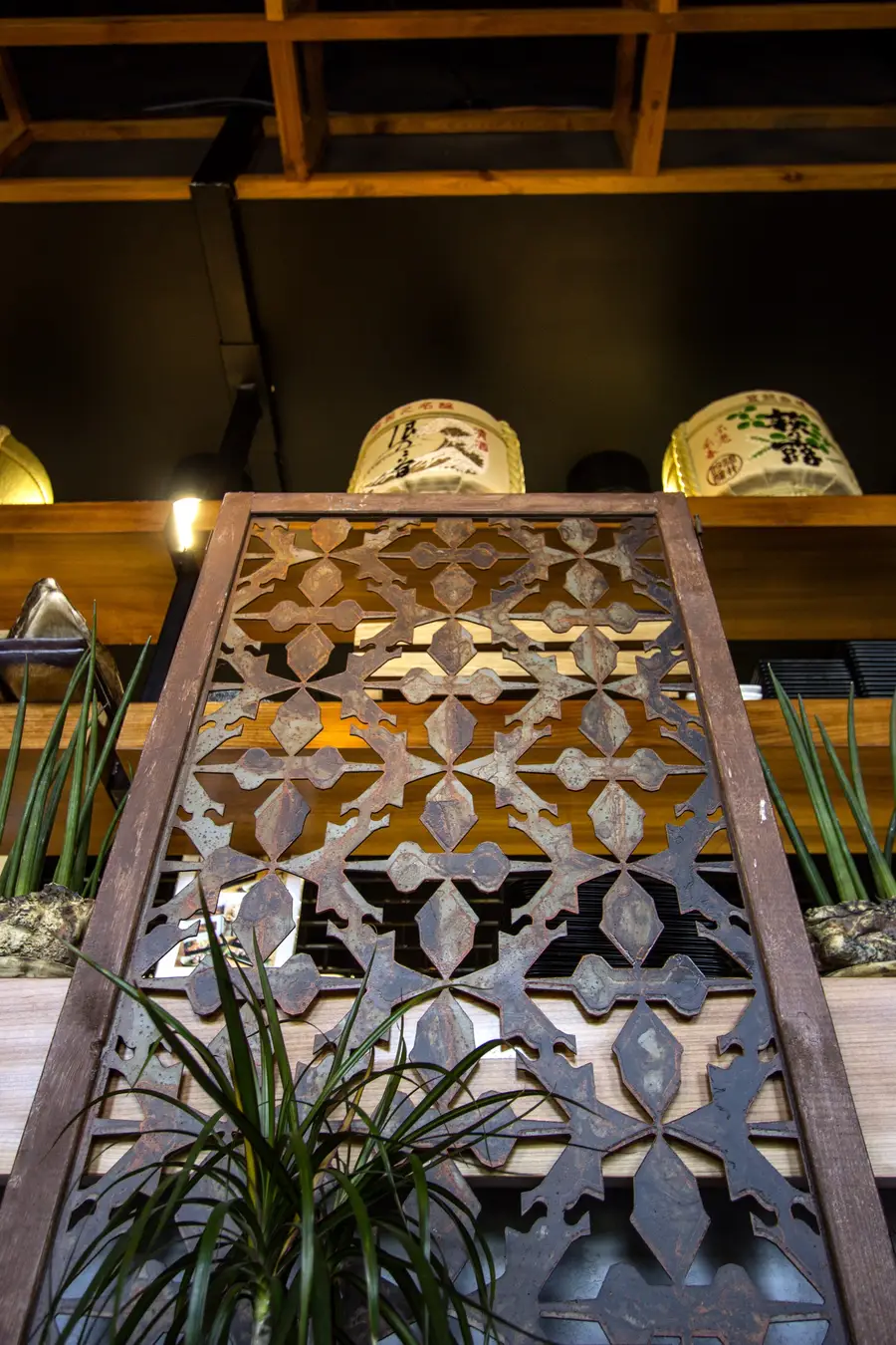 Interior: metal screen panel close-up from below, sake barrels on shelf above, lattice ceiling