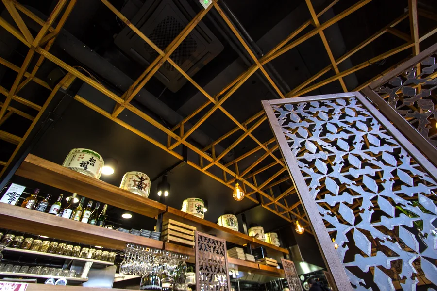 Interior: bar shelves close-up from below — sake barrel displays, ceiling lattice, metal screens