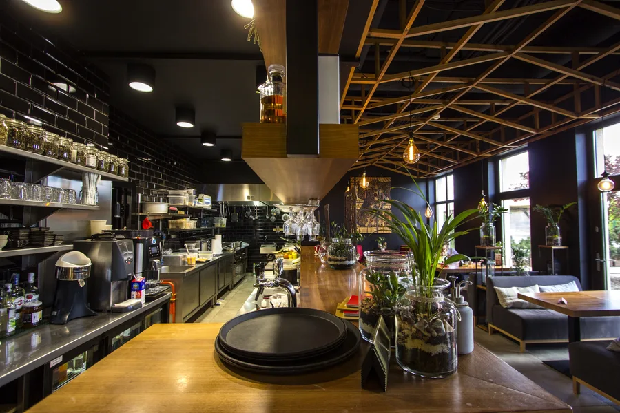 Interior: open kitchen from behind counter — equipment, black tile walls, prep area, dining floor beyond