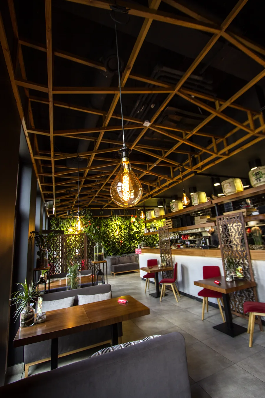 Close-up dining zone: teardrop pendant globe, ceiling lattice, bar shelves, metal screens, warm golden light, evening