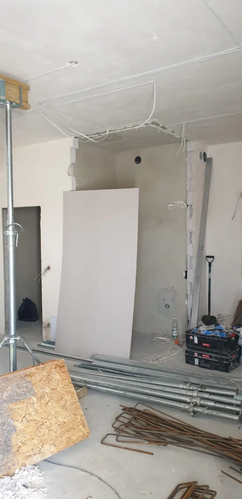 Interior during structural works with new partition walls, steel acrow prop supporting ceiling, exposed electrical wiring, drywall board and rebar bundles on floor